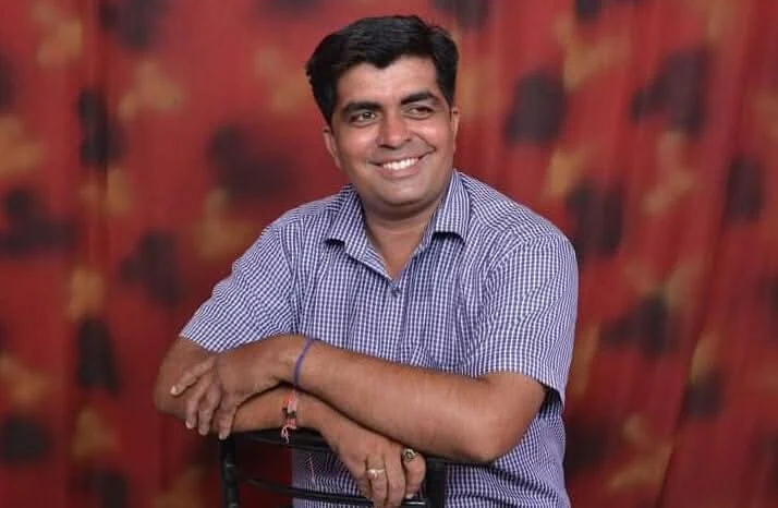 Dr. Avadhesh Kaushik in a relaxed seated pose leaning on a chair