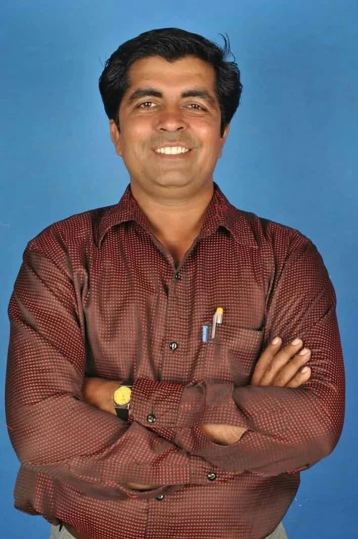 Dr. Avadhesh Kaushik standing with crossed arms against a blue background