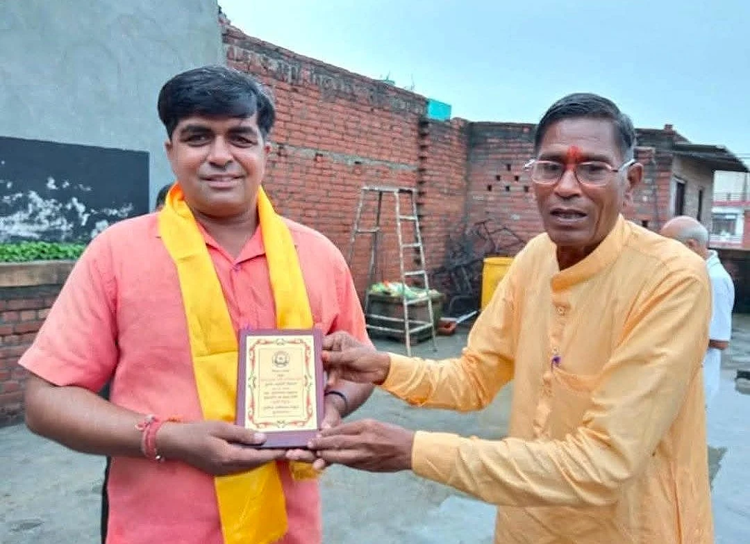 Dr. Avadhesh Kaushik receiving a wooden felicitation plaque from a senior elder